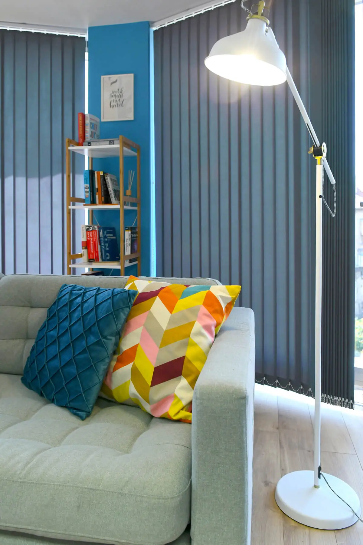 A close photograph of the couch, standing lamp, and a small library in the relax room in the Parachut office.